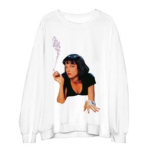 May include: White sweatshirt with a graphic of a woman with black hair and a black top, smoking a cigarette. The image has a vintage, artistic style. The sweatshirt has long sleeves and a crew neck.