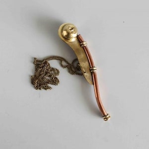 May include: A vintage whistle featuring a brass head and accents, a copper body, and a brass chain. The whistle has a curved design, likely used for signalling or as a decorative item.
