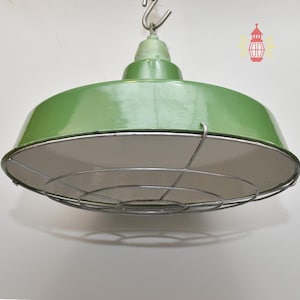 May include: A green, industrial-style pendant light with a metal cage and a white interior. The light fixture is suspended from a hook and has a glossy finish. The overall design is vintage and functional.