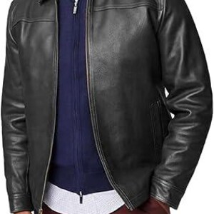 May include: A black leather jacket with a collared neckline and a front zip. The jacket is layered over a navy blue zip-up sweater and a white and blue patterned shirt. The person is wearing burgundy trousers.