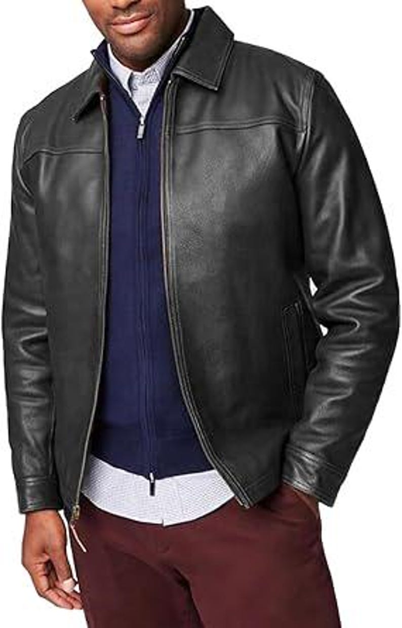 May include: A black leather jacket with a collared neckline and a front zip. The jacket is layered over a navy blue zip-up sweater and a white and blue patterned shirt. The person is wearing burgundy trousers.