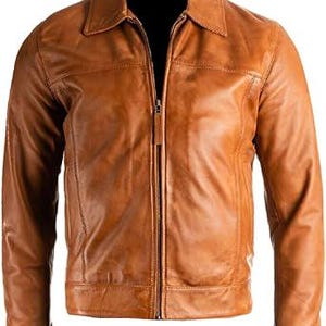 May include: A tan leather jacket featuring a collared neckline and a full-length zip. The jacket has long sleeves and a tailored fit, with visible stitching details. The leather has a slightly distressed appearance.