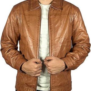 May include: A brown leather jacket with a zip fastening. The jacket features a collared neckline and a textured finish. The model is wearing a white t-shirt underneath.