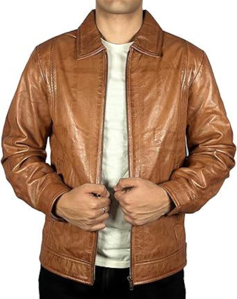 May include: A brown leather jacket with a zip fastening. The jacket features a collared neckline and a textured finish. The model is wearing a white t-shirt underneath.