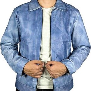 May include: A pale blue leather jacket with a zip-up front and a collared neckline. The jacket has a distressed look and is worn over a white t-shirt. The model is wearing black trousers.
