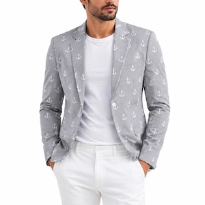 Op de afbeelding: Een lichtgrijze blazer met een herhalend wit ankerpatroon, een ingekeepte revers en een sluiting met één knoop. De blazer wordt gedragen over een effen wit T-shirt en gecombineerd met een witte broek, wat een nautisch geïnspireerd ensemble vormt.