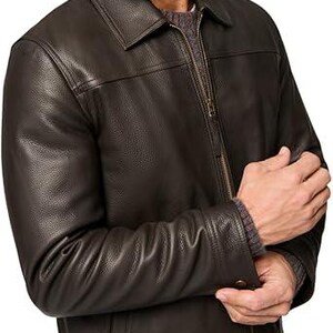 May include: A dark brown leather jacket with a collared neckline and a zip fastening. The jacket has a textured finish and buttoned cuffs. The sleeves are long and the jacket appears to be well-fitted.