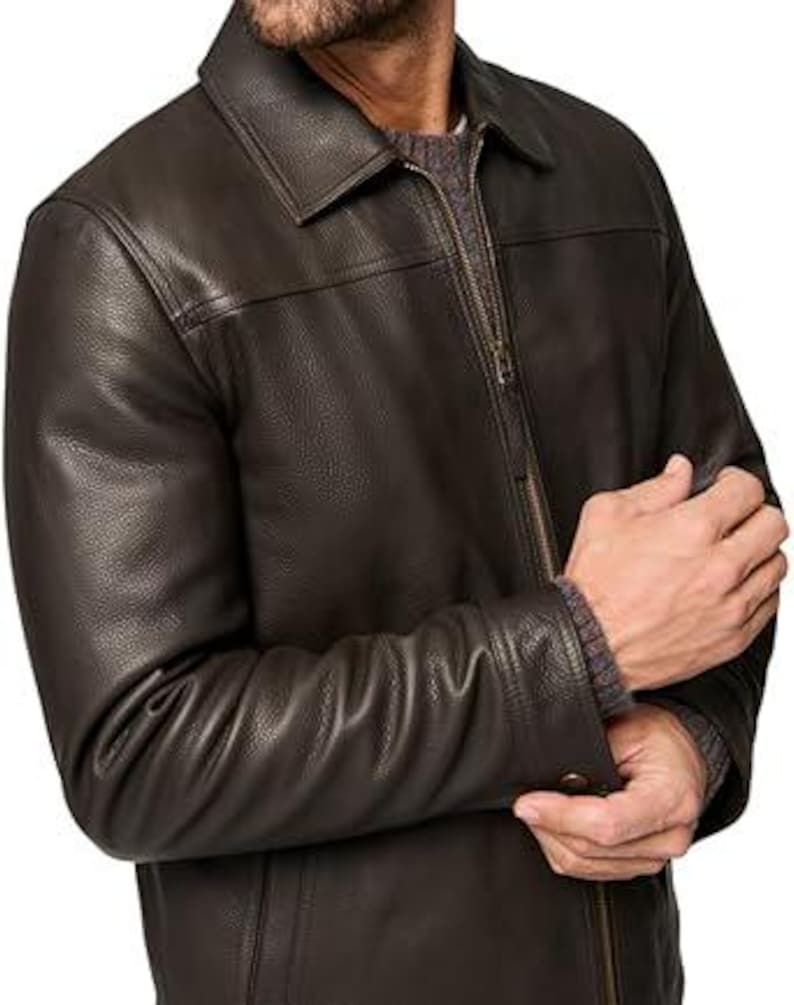 May include: A dark brown leather jacket with a collared neckline and a zip fastening. The jacket has a textured finish and buttoned cuffs. The sleeves are long and the jacket appears to be well-fitted.