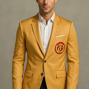 Puede incluir: Blazer amarillo mostaza con un emblema rojo y dorado en el pecho. El blazer tiene solapas con muescas, dos bolsillos delanteros y un pañuelo blanco. El modelo lleva una camisa blanca y pantalones negros.