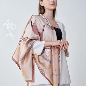 May include: A silk scarf with a horse and equestrian-themed design in shades of beige, brown, and gold. The scarf is draped over a white blazer and black top. The scarf's edges are trimmed with a dark brown border.