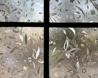 May include: Decorative window film with a floral pattern. The film features a repeating design of leaves and flowers in shades of silver and gray. The film is divided into four sections by black lines.