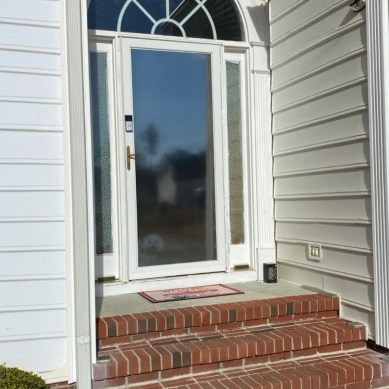 May include: A white front door with a glass storm door and a welcome mat. The door is surrounded by white siding and there are brick steps leading up to the door.