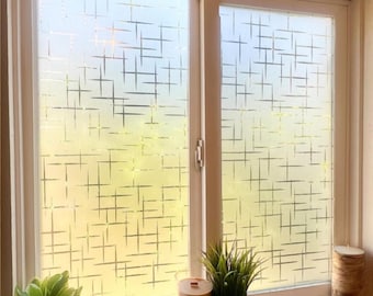 May include: A window with a white frame and a frosted glass design featuring a pattern of intersecting lines. The window is partially open, and the interior is visible. A small plant, a candle, and a potted plant sit on the windowsill.