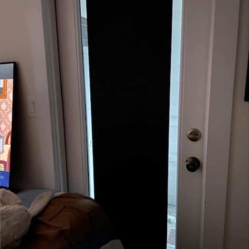 May include: A white door with a black blackout curtain covering the window. The door has two silver door knobs.