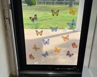May include: A glass door decorated with various butterfly stickers in shades of orange, yellow, blue, and brown. The butterflies are arranged across the glass, with a view of a green lawn and trees visible through the door.