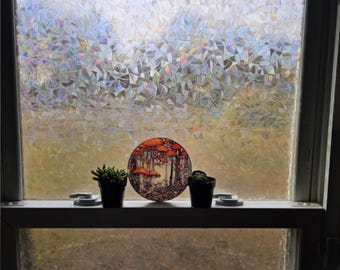 May include: A window with a decorative privacy film featuring a geometric pattern. Two small potted plants and a round plate with a mushroom design are on the window sill.