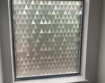 May include: A window with a geometric pattern of triangles. The triangles are in shades of silver and gray, creating a textured, iridescent effect. The window is framed in black and set in a white frame.