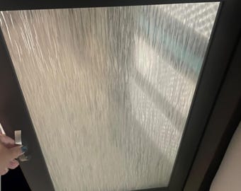 May include: A dark brown cabinet door with a textured glass panel. The door is slightly ajar, revealing a glimpse of the interior. A hand is reaching for the silver handle.
