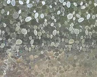 May include: A close-up view of a textured surface covered in small, oval-shaped stones. The stones vary in color, with shades of gray, white, and brown. The arrangement creates a natural, organic pattern, suitable for decorative applications.