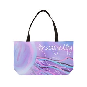 Puede incluir: Un bolso tote con asa negra y diseño colorido. El bolso presenta una ilustración de medusa en tonos morados, rosas y azules, con la palabra "transjelly" escrita en cursiva.