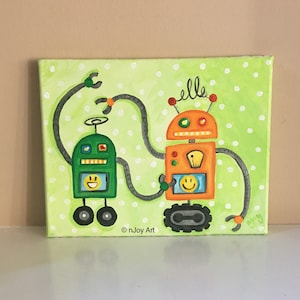 May include: A green and orange robot painting on a green canvas with white polka dots. The robots are holding hands and smiling. The painting is signed "nJoy Art".