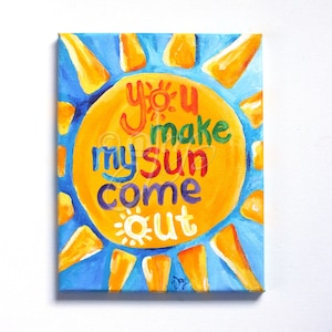 May include: A yellow sun with a blue sky background and the words "you make my sun come out" written in rainbow colors.