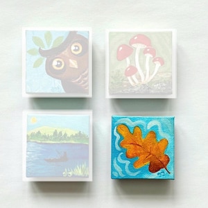May include: Four small square canvases featuring painted scenes: an owl with green leaves, a cluster of pink mushrooms, a landscape with a person in a canoe on a lake, and a single orange oak leaf against a bright blue background with wavy lines.