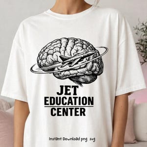 May include: White t-shirt with a black and white graphic. The design shows a brain with a jet plane circling it, and the text "JET EDUCATION CENTER" underneath. The phrase "Instant Download png svg" is at the bottom of the design.
