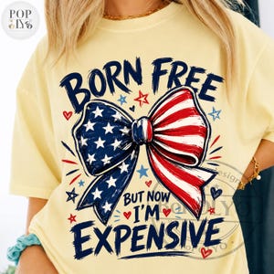 May include: Yellow t-shirt with a patriotic bow design. The bow features the American flag with red and white stripes and blue stars. Text reads "BORN FREE BUT NOW I'M EXPENSIVE."
