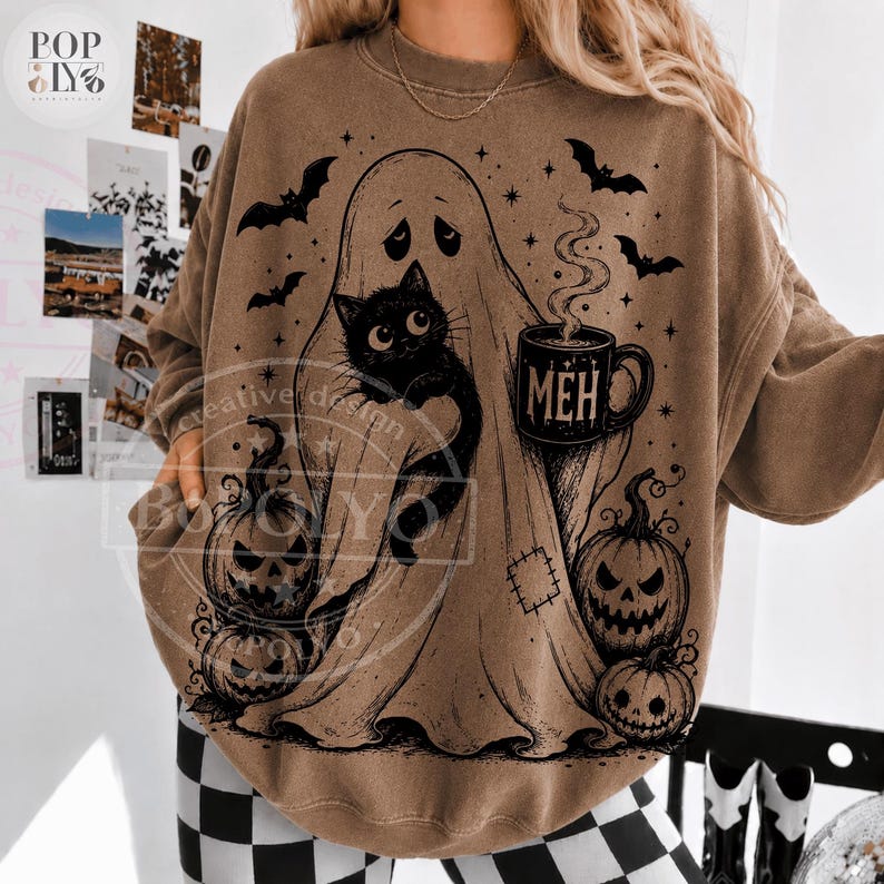 Puede incluir: Una sudadera marr&oacute;n de cuello redondo con un estampado gr&aacute;fico negro de un fantasma sosteniendo un gato negro y una taza humeante con la palabra MEH. El dise&ntilde;o incluye tres calabazas, varios murci&eacute;lagos volando y peque&ntilde;as estrellas.