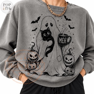 Puede incluir: Una sudadera gris carb&oacute;n de cuello redondo con un gr&aacute;fico en tinta negra de un fantasma sosteniendo un gato negro y una taza humeante con la palabra "MEH". El dise&ntilde;o incluye murci&eacute;lagos, estrellas y tres calabazas con rostros tallados.