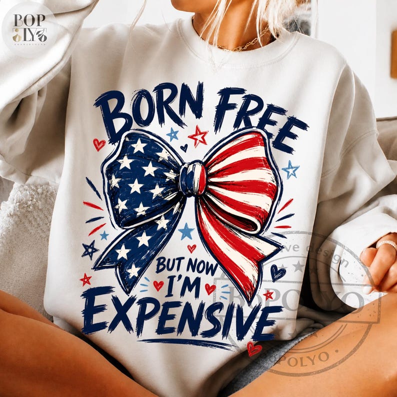 May include: White sweatshirt with a patriotic bow design. The bow features a blue section with white stars and a red and white striped section. The text "BORN FREE BUT NOW I'M EXPENSIVE" is printed below the bow.