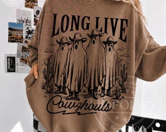 Puede incluir: Una sudadera marrón de cuello redondo con un estampado gráfico negro de cuatro fantasmas con sombreros de vaquero en un paisaje desértico con cactus. El texto "LONG LIVE" aparece sobre los fantasmas y "Cowghouls" debajo de ellos.