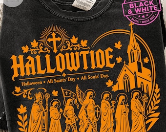 May include: A charcoal gray crewneck sweatshirt featuring a vibrant orange graphic print. The design displays the text HALLOWTIDE, Halloween, All Saints' Day, All Souls' Day, a church silhouette, and a procession of figures with religious iconography.