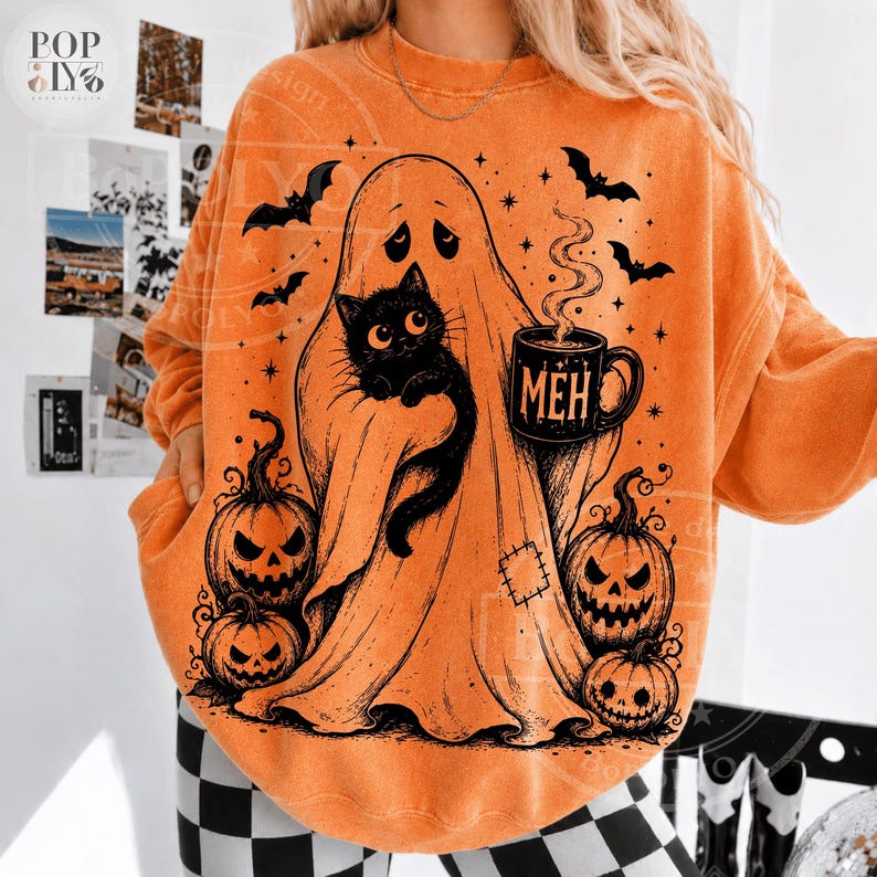 Puede incluir: Una sudadera naranja de cuello redondo con un estampado gr&aacute;fico negro de un fantasma sosteniendo un gato negro y una taza con el texto MEH. El dise&ntilde;o incluye tres calabazas de Halloween, murci&eacute;lagos voladores y peque&ntilde;as estrellas.