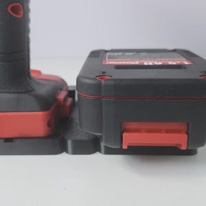 May include: A black and red power tool with a battery pack. The tool has a black handle with a red accent and a red button. The battery pack is black with a red accent and a red release latch.