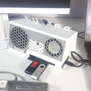 May include: A white computer cooling device with a grey honeycomb grill design and USB ports. Several USB flash drives are inserted into the device. A laptop and keyboard are also visible.