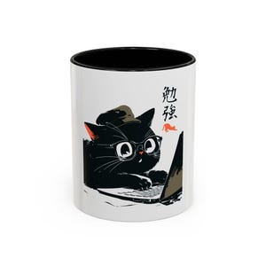 May include: A white ceramic mug with a black interior and rim, featuring a graphic illustration of a black cat wearing glasses and a cap while using a laptop. The design includes the Japanese kanji characters for study and a small orange cat icon.