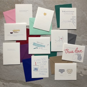 May include: A collection of greeting cards with various humorous and romantic messages. The cards feature illustrations of a heart, a couple, a gas station drink, a bathroom, and a trash can. The cards are printed on white cardstock and have a variety of colors, including red, blue, green, and brown.