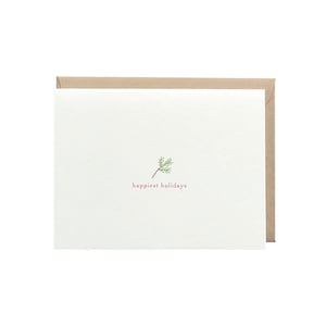 May include: A white card with a small green sprig and the text "happiest holidays" in pink.
