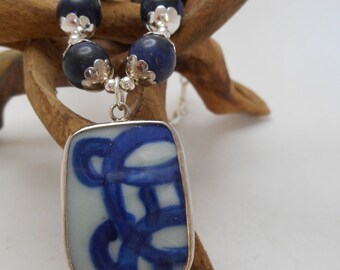 May include: A silver necklace with a blue and white porcelain pendant and blue gemstone beads.