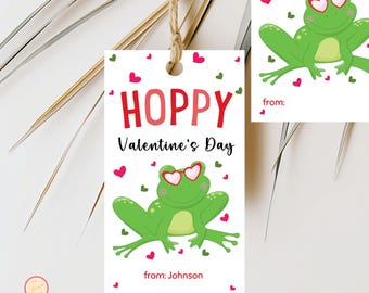 Peut inclure: Une étiquette cadeau de Saint-Valentin avec une grenouille verte portant des lunettes en forme de cœur. Le texte "HOPPY Valentine's Day" est en rouge, avec "from: Johnson" en bas. Des cœurs roses et verts décorent l'étiquette.