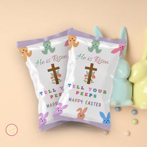 May include: Two white bags with purple trim, filled with candy. The bags have a cross with flowers, and the text "He is Risen" and "Tell Your Peeps Happy Easter".
