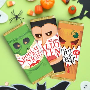 May include: Three rectangular chocolate bars with Halloween-themed wrappers. The green wrapper features a monster face and the text Spooky Night. The center wrapper shows a vampire with the text happy HALLOWEEN. The orange wrapper depicts a jack-o'-lantern with the text trick or treat.