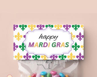 Op de afbeelding: Een transparante cellofaan zak gevuld met kleurrijke snoepjes, bekroond met een decoratieve kaart. De kaart toont de woorden "happy MARDI GRAS" in een witte, geschulpte lijst, omringd door groene, gouden en paarse fleur-de-lis symbolen.