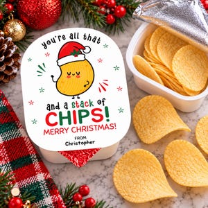 May include: A white rectangular snack container lid featuring a cartoon potato wearing a Santa hat, with the text: You're all that and a stack of CHIPS! MERRY CHRISTMAS! FROM Christopher. Several golden yellow potato chips are visible inside and outside.