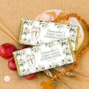 Op de afbeelding: Twee chocoladereepverpakkingen met bloemen- en kruisontwerpen. De verpakkingen lezen "Samantha's Eerste Heilige Communie" met een datum. Witte lelies en een rozenkrans met een kruis zijn te zien. De achtergrond bevat brood, pruimen en een rozenkrans.