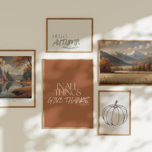 May include: A collection of framed art prints with autumn themes. The prints include landscape paintings, a pumpkin outline, and text that reads "Hello Autumn" and "In All Things Give Thanks". The frames are a light brown color.