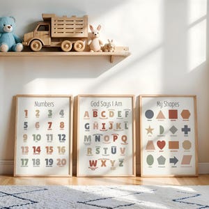 May include: Three framed educational posters with the text "Numbers", "God Says I Am", and "My Shapes". The posters are in a light wood frame. A wooden toy truck, a blue teddy bear, and two stuffed rabbits sit on a shelf above the posters.