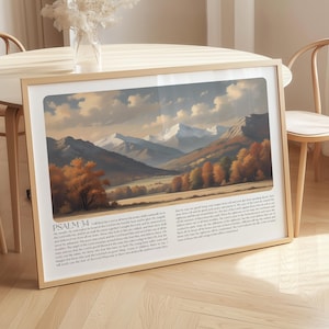 May include: Framed landscape art print featuring a mountain range with snow-capped peaks, a valley, and autumn-colored trees. The artwork is in a rectangular frame with a light wood finish. Text from Psalm 34 is printed at the bottom.